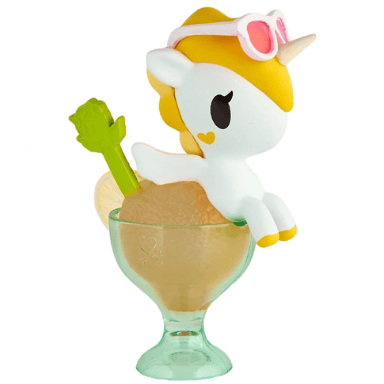 A tokidoki Shaved Ice Dreams Unicorno Blind Box figure—featuring a toy unicorn with yellow hair, pink sunglasses, and a heart on its cheek—sits playfully on the rim of a dessert glass filled with a light brown icy treat and accompanied by a green spoon, making it an irresistible collectible for fans of whimsical toys.