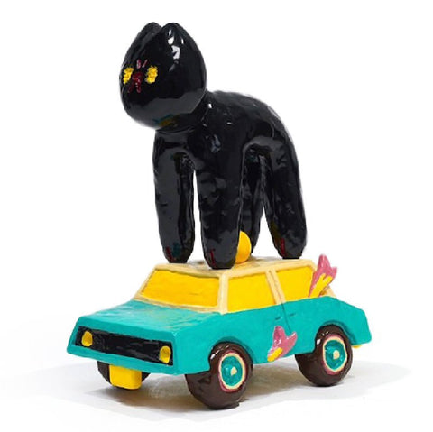 A colorful ceramic sculpture, The Cat Car by How2Work (HK), features a black cat standing on top of a teal car with yellow windows and pink birds attached to its sides.