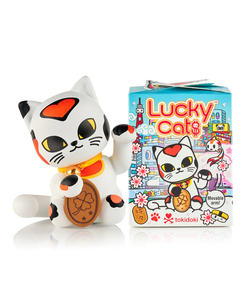 A tokidoki (IT) Lucky Cats figurine waves beside a Tokidoki Lucky Cats Blind Box, which features collectible kitty illustrations and the tokidoki logo.