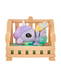 A tokidoki Baby Unicorno Blind Box figure in pastel colors lies on its back in a tan crib, holding a bottle—an adorable collectible perfect for any surprise unboxing.