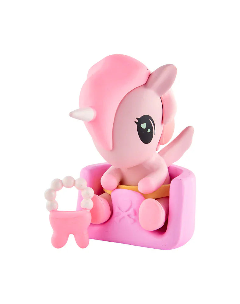 A pink unicorn figurine with a white horn sits in a pink chair, holding a pink and white beaded accessory—an adorable collectible from the tokidoki Baby Unicorno Blind Box series by tokidoki, perfect for any collector.