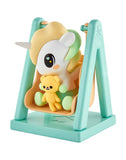 A tokidoki Baby Unicorno Blind Box figurine featuring a teddy bear sits on a peach and mint green swing—perfect for collectible figure fans—shown against a white background.
