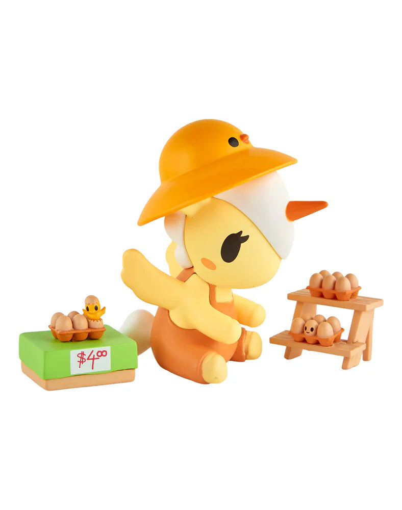 A yellow cartoon figure in an orange hat sits with toy eggs on a green 