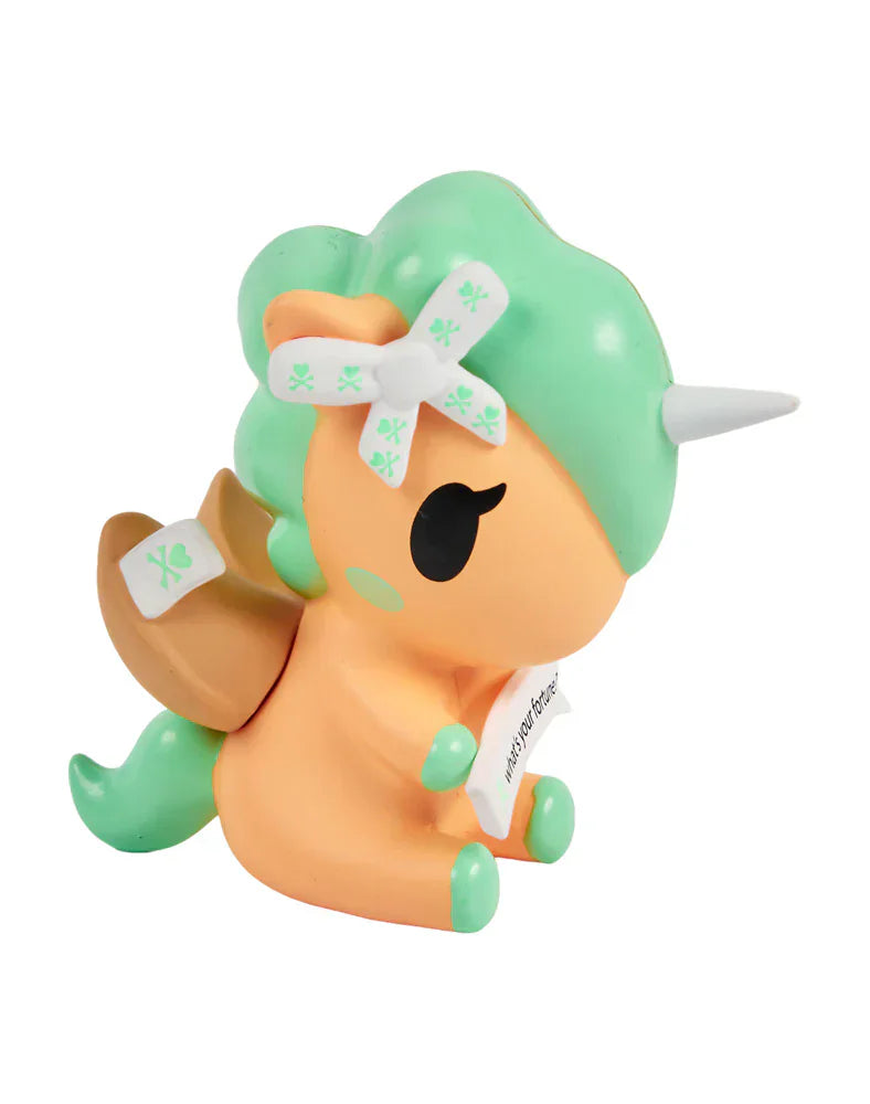 The Tokidoki Fortune Cookie Unicorno Blind Box features a small orange and green figure with a white horn, brown wings, and a scroll in its mouth—an adorable collectible surprise!.