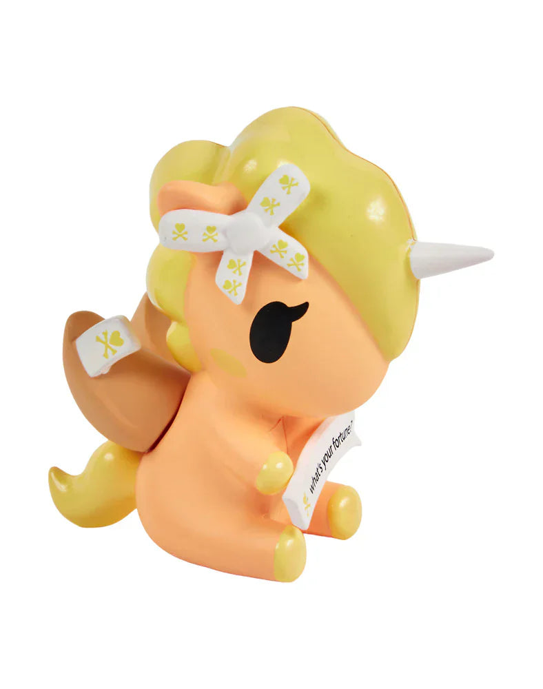 Discover Tokidoki’s Fortune Cookie Unicorno Blind Box: a small, orange-and-yellow figurine with a white horn, yellow skull bows, wings, and a scroll — an adorable surprise collectible!.