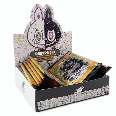 A display box containing The Monsters Trading Card Series 2 by How2Work (HK). The box, part of The Monsters series, features artwork of a black and white character with colorful eyes. Several packs are arranged in the box.