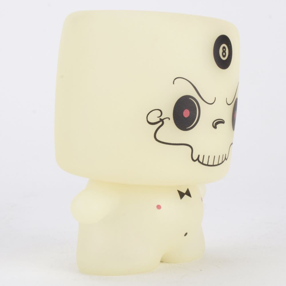 Introducing the Grim Marshall by 64 Colors, a limited edition figure from Squibbles Ink + Rotofugi (US). This collectible boasts a beige vinyl body and a square head featuring a cartoonish skull face adorned with an eight ball symbol on top. A small bow tie adds an extra touch of charm, while its glowing visage brings an element of mystique to any collection.