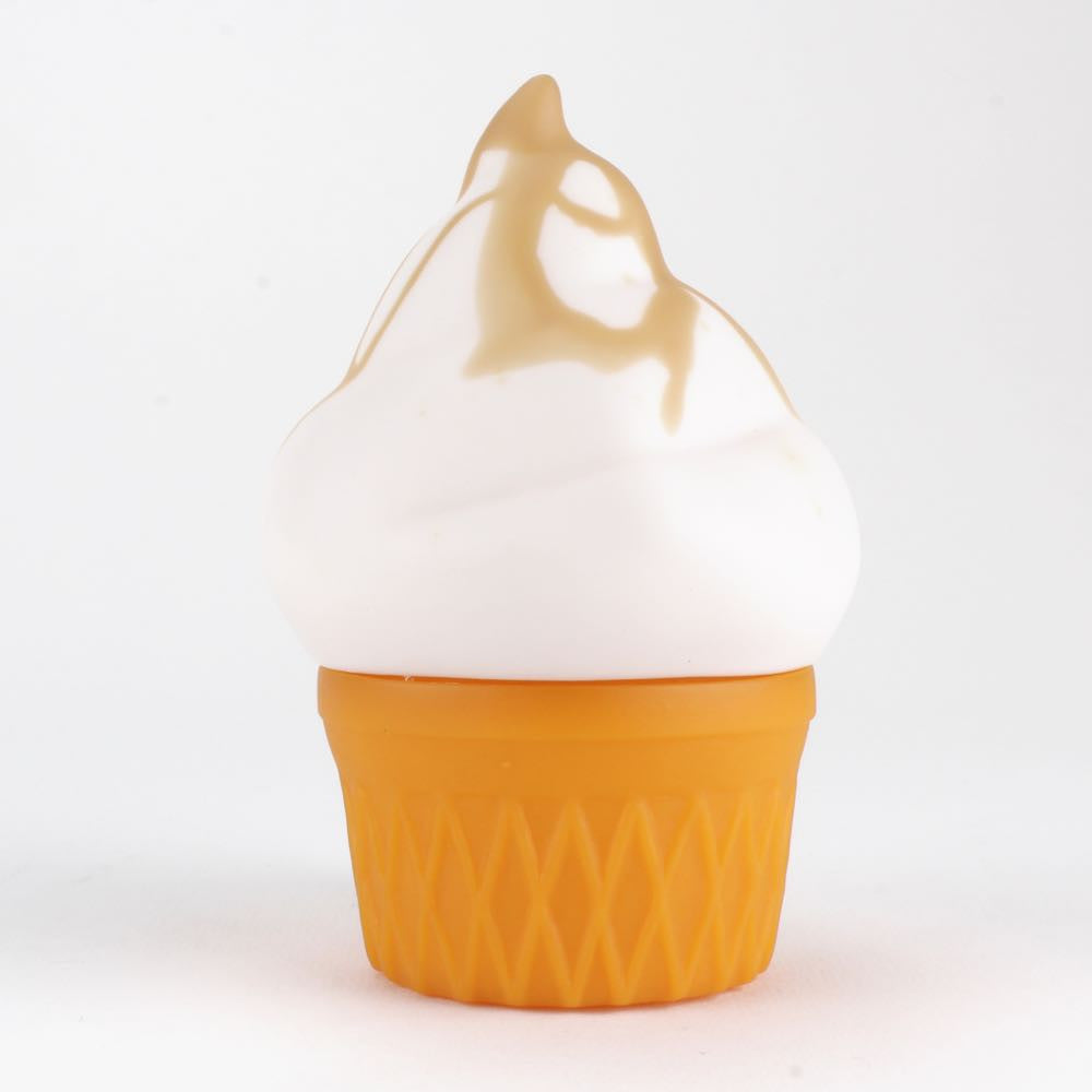 A soft-serve ice cream in a cone with caramel drizzle evokes the Smorkin' Monger Jerome by Squibbles Ink + Rotofugi, striking like a Frank Kozik special edition against a plain backdrop.