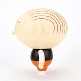 A side view of the Jimmy Corrigan Vital Animus Vinyl Doll by Presspop (JP)—a cartoonish figure with a large bald head, black lines for hair, black vest, white shirt, orange pants, and white shoes inspired by Chris Ware’s acclaimed comics.