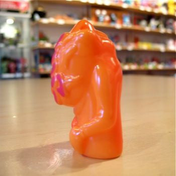 An orange Popsoda Finger Puppet toy, possibly a kaiju, rests on a table in a store.
