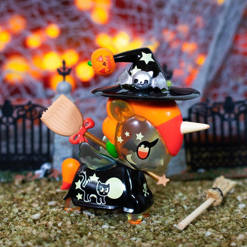 A Unicorno After Dark Series 2 Blind Box toy from tokidoki stands in front of a graveyard with her broom.