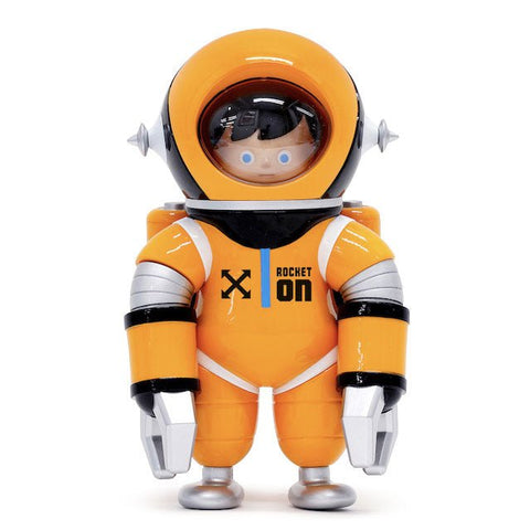 A Unio — Rocket On astronaut toy in an orange suit stands on a white background, capturing the retro aesthetic.